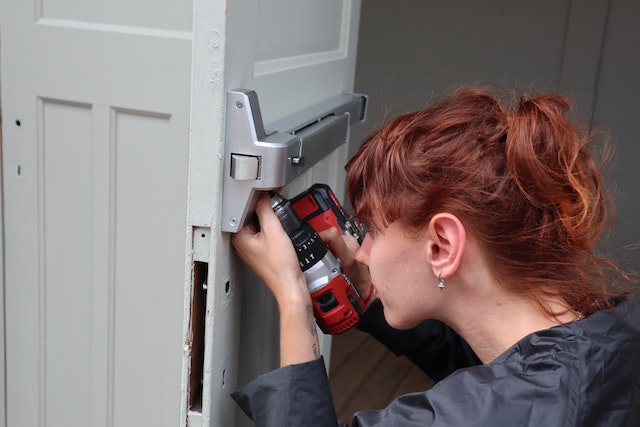 person-using-a-drill-to-fix-the-hinge-on-an-emergency-exit-door
